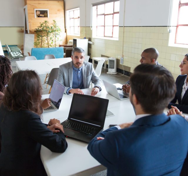 Confident leader talking to subordinates. Concentrated workers sitting at table and listening boss. Business meeting concept